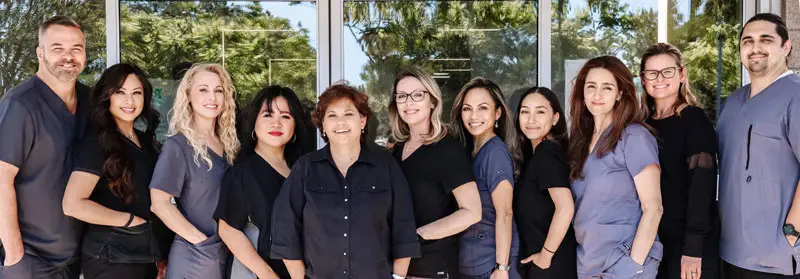 Group of smiling healthcare professionals standing together outside a clinic, wearing uniforms and business attire