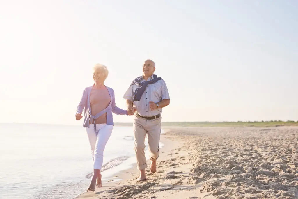 an older couple barefoot running on the beach