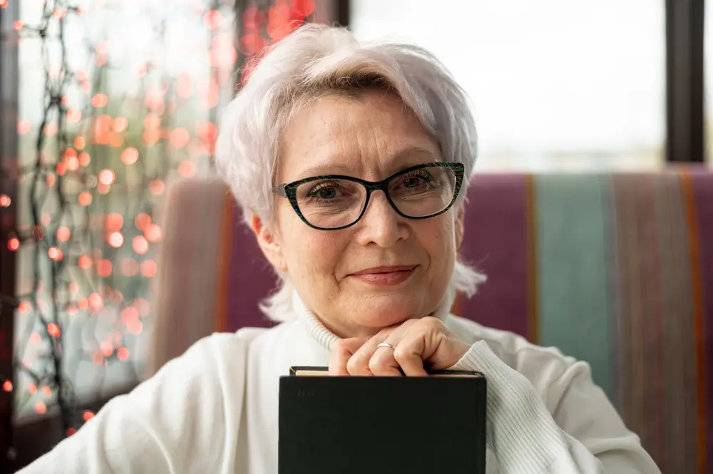front view senior female with glasses holding a book while smiling